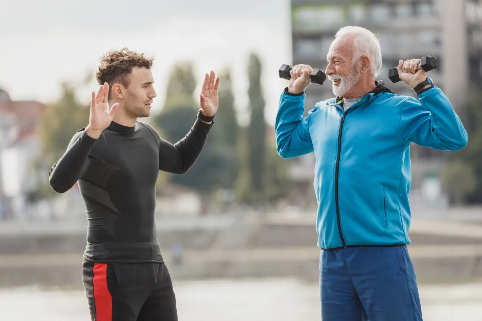 Hombre mayor y su entrenador levantando mancuernas frente al río