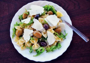 Plato de ensalada de pasta con queso, aceitunas y verduras sobre una mesa