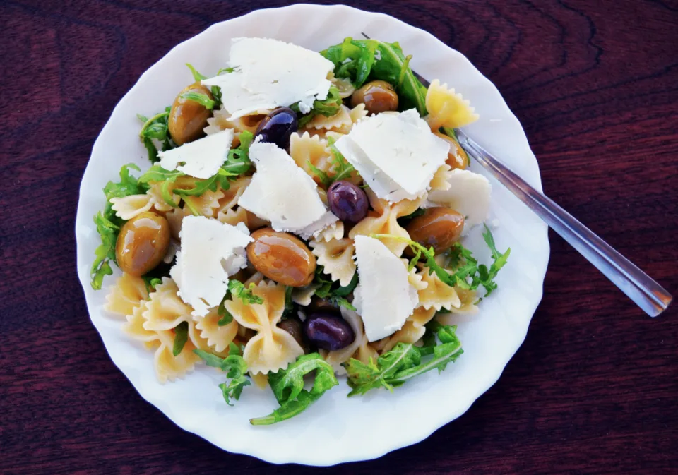 Plato de ensalada de pasta con queso, aceitunas y verduras sobre una mesa